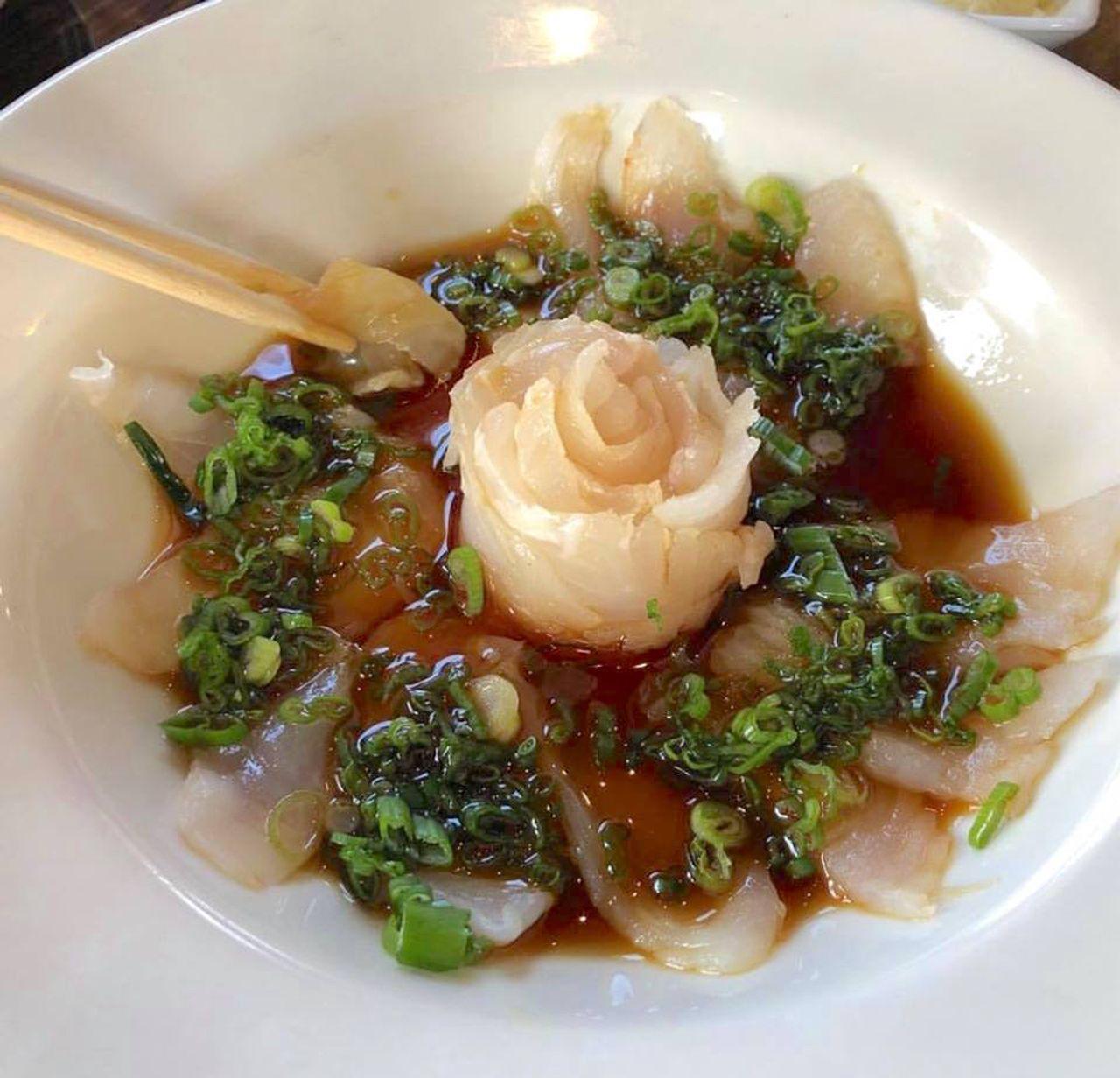 Sliced sashimi with ginger rose, green onions, and soy sauce in a white bowl.
