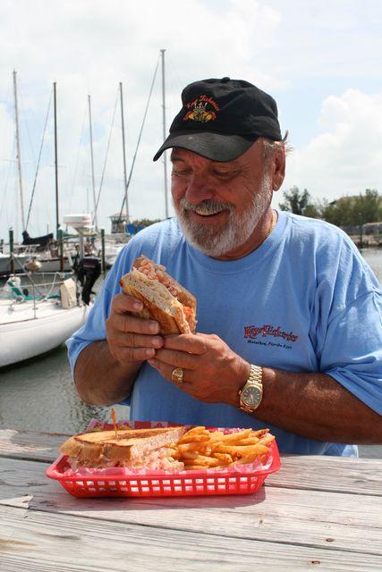 Older man enjoying a sandwich and fries at a seaside table.
