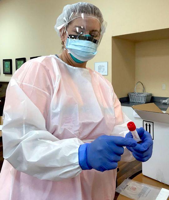 Healthcare worker in PPE holding a test tube in a clinical setting.