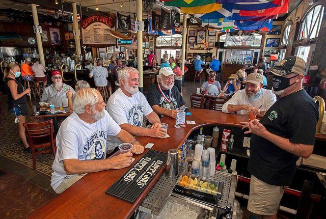 Men with beards wearing white shirts sit at a bar counter, chatting with the bartender.