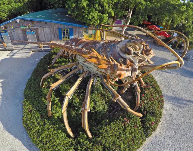 Giant lobster sculpture surrounded by greenery, near a wooden building.