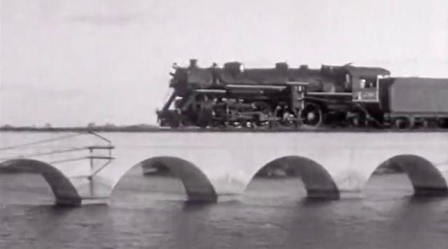 Steam train crossing an arched bridge over water.