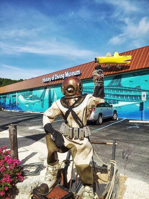 Diver statue holding a yellow submarine in front of a museum.