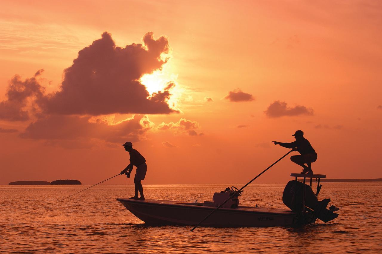 Silhouetted fishers on a boat during a vibrant orange sunset.