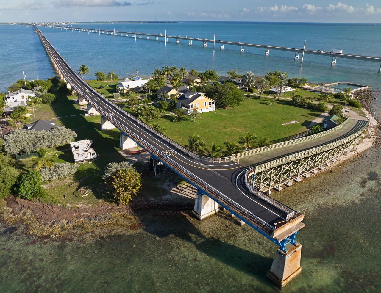 Aerial view of a long bridge over ocean, connecting green land areas.