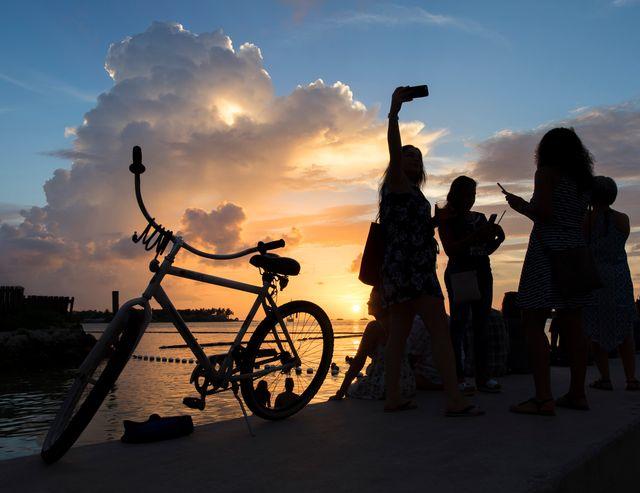Silhouettes of people and a bike by a sunset over water.