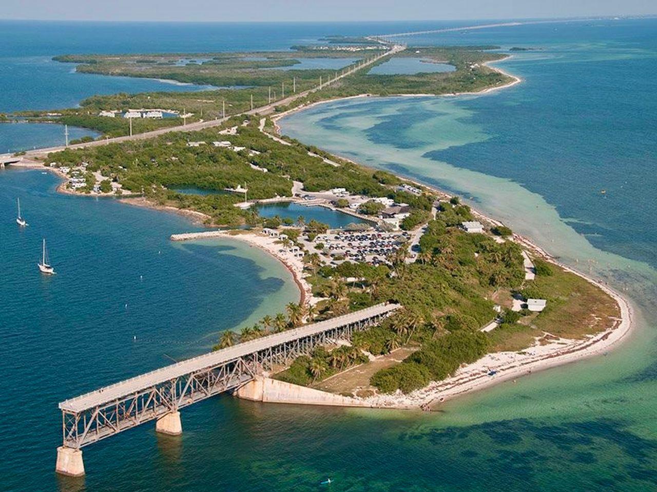 Aerial view of a coastal island with greenery and a long bridge.