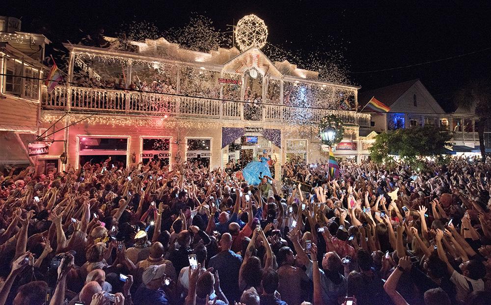 Crowd celebrating with lights at night, large building decorated in the background.
