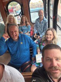People smiling on a bus, casually dressed, with seating visible.