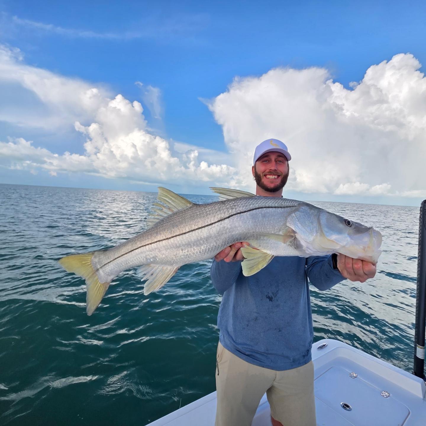 Man on boat holding large fish under blue sky.