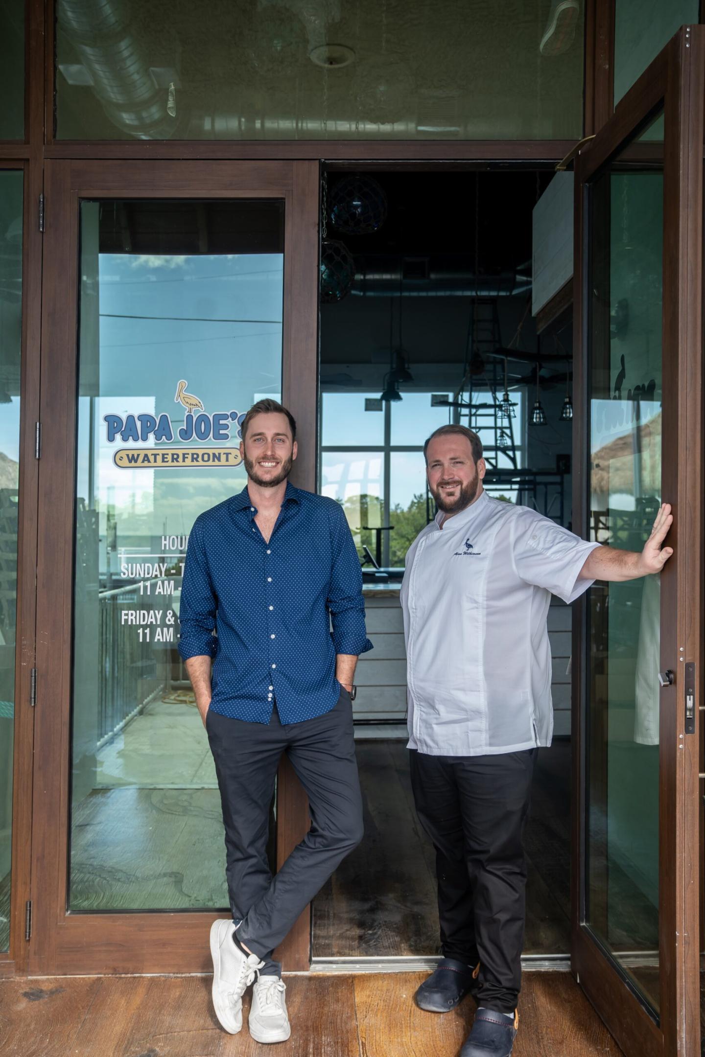 Two men smiling in front of a restaurant entrance.