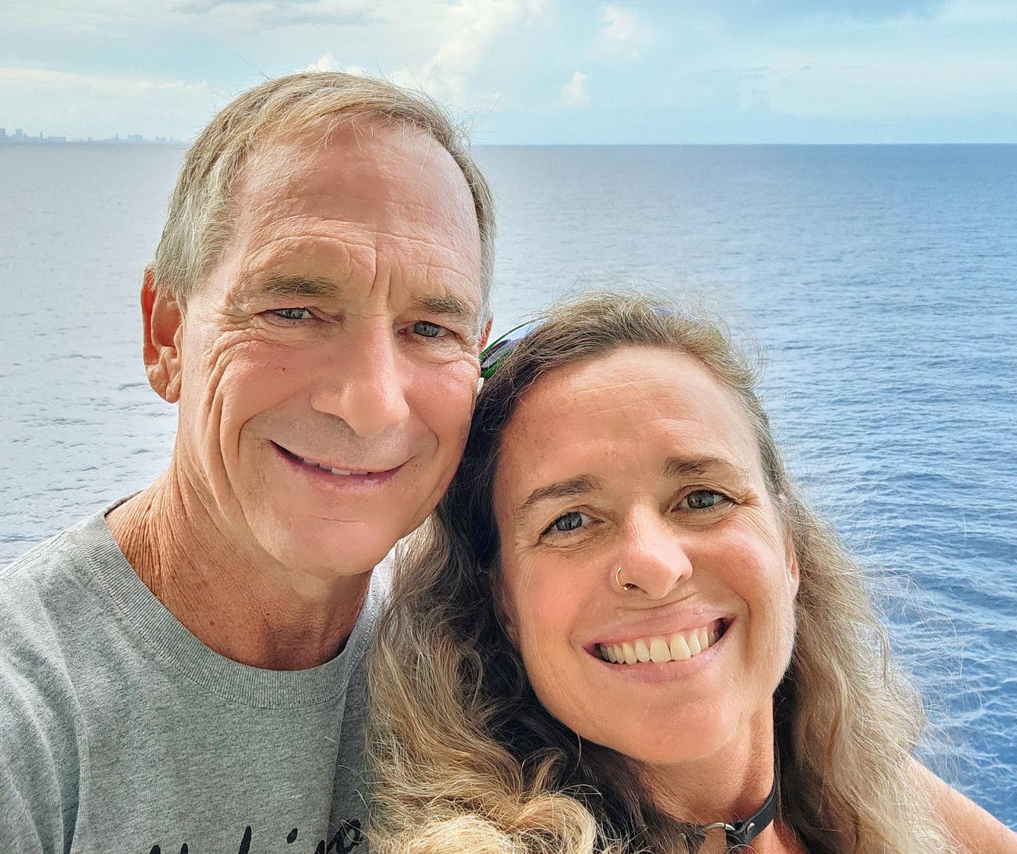 Smiling couple in front of the ocean, clear sky in the background.