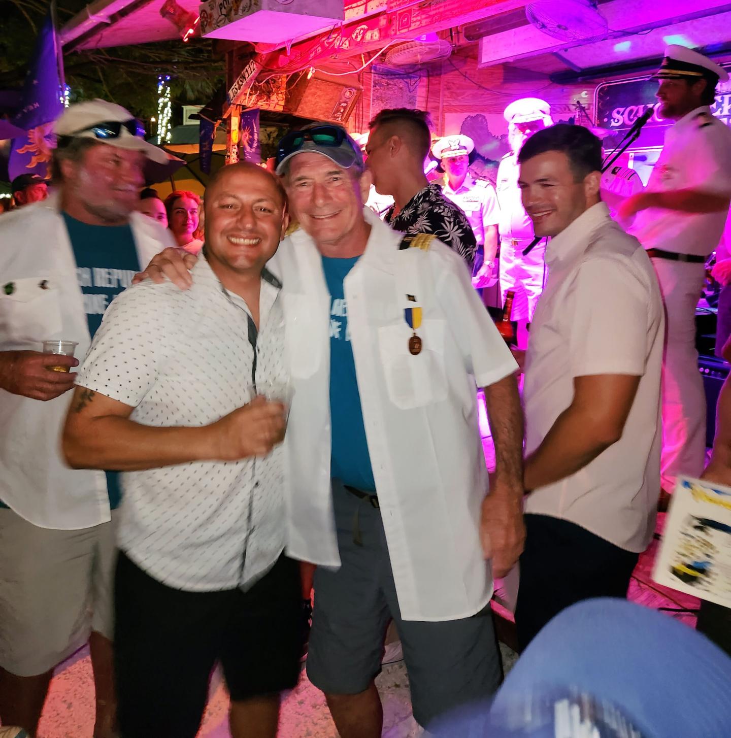 Men smiling and posing at a lively party with neon lights and a nautical theme.
