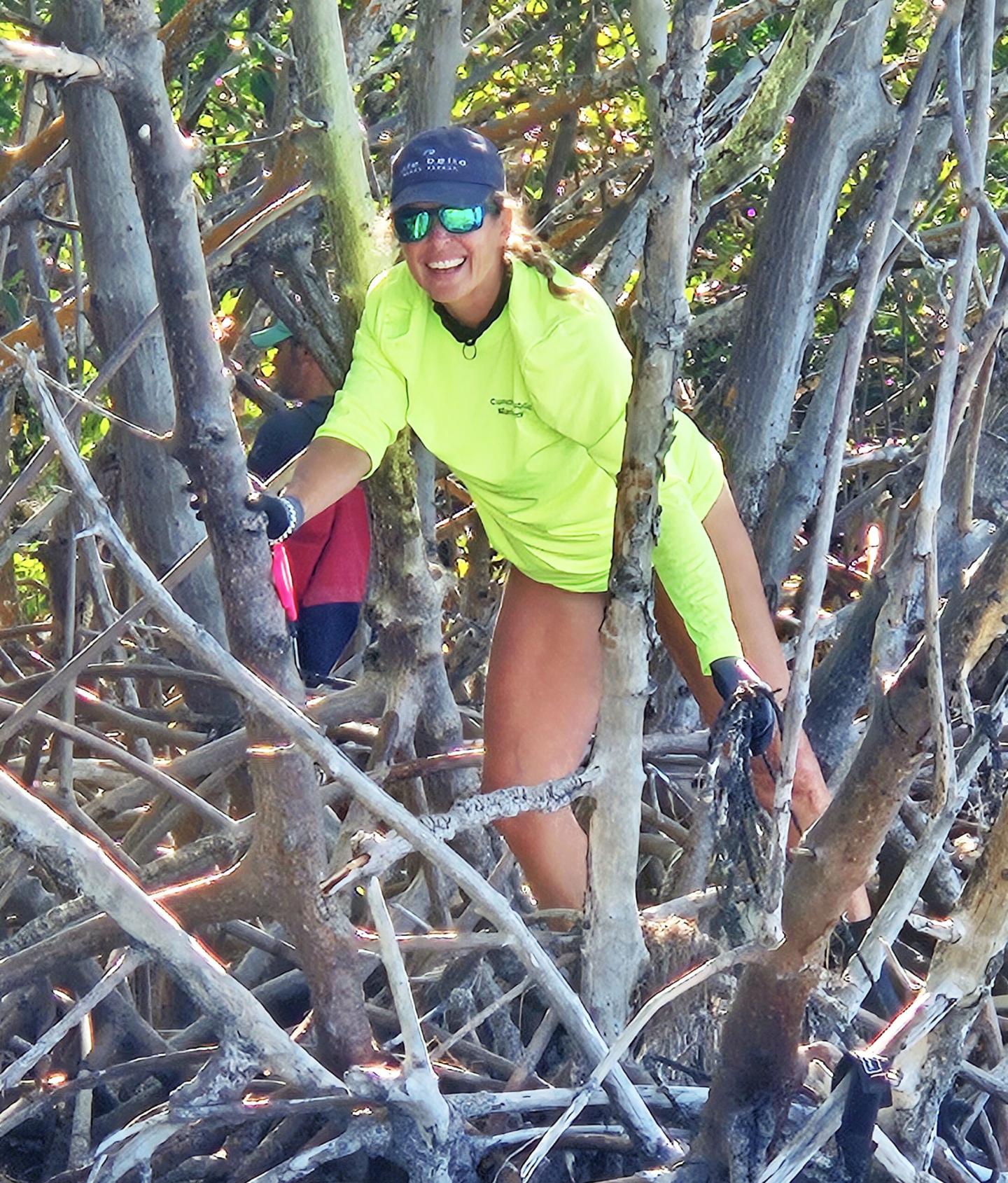 Person smiling and climbing among tree branches, wearing a bright green shirt and cap.