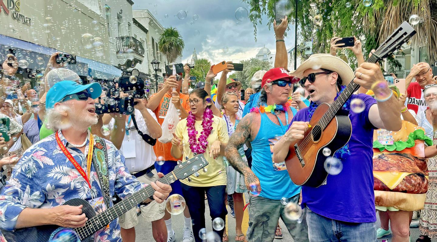 Musicians playing guitars in a festive crowd at a street event with bubbles.