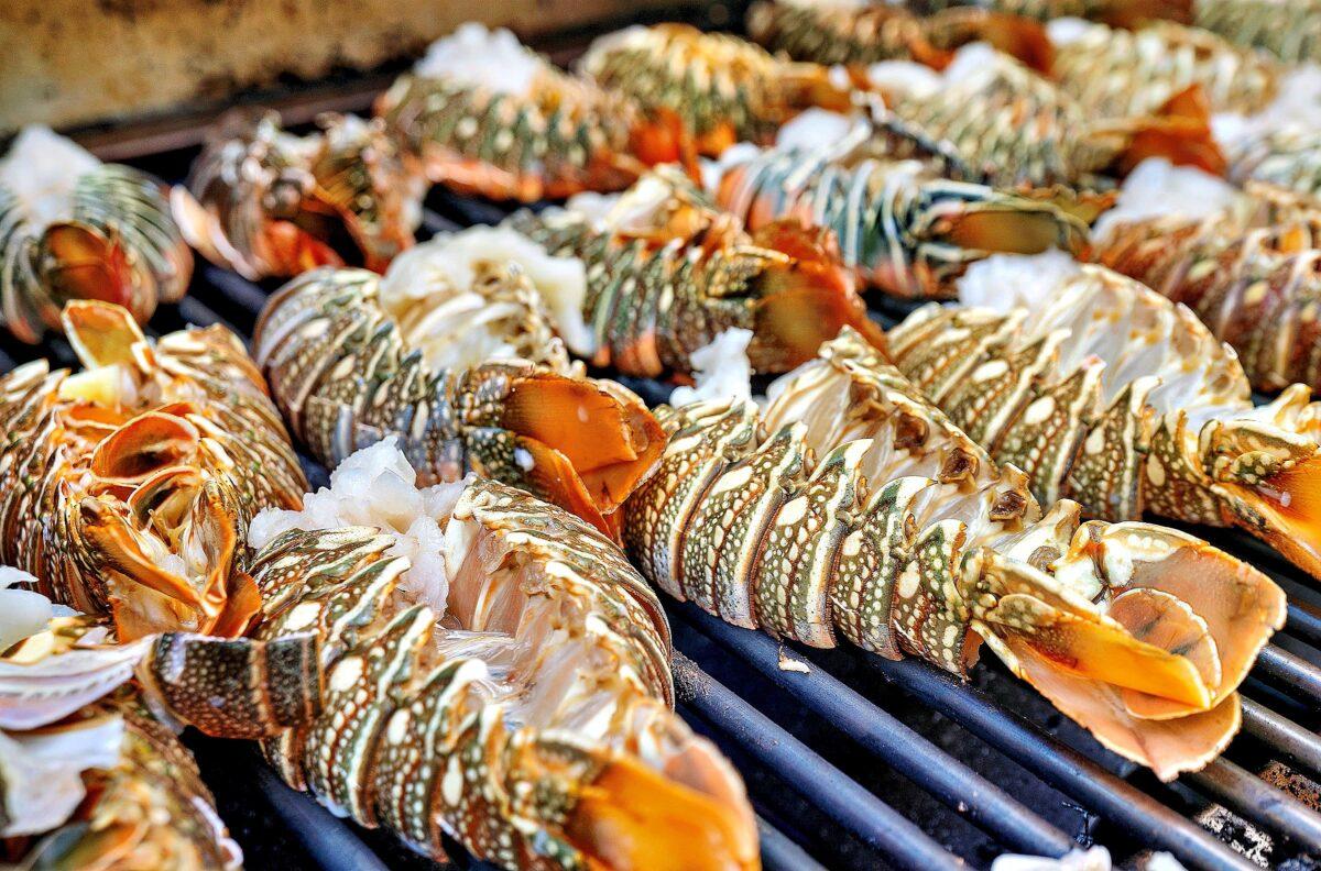 Grilled lobster tails on a barbecue, shells golden with white meat exposed.