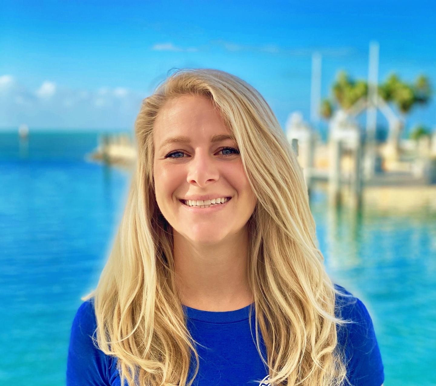 Smiling woman by a bright blue sea and clear sky.
