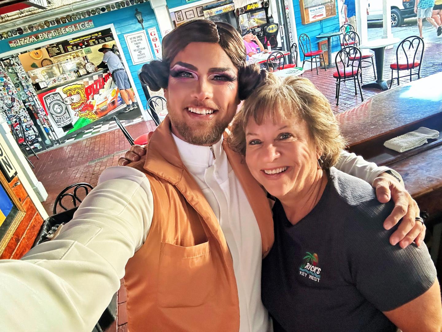 Two people smiling and posing for a selfie in a colorful cafe.