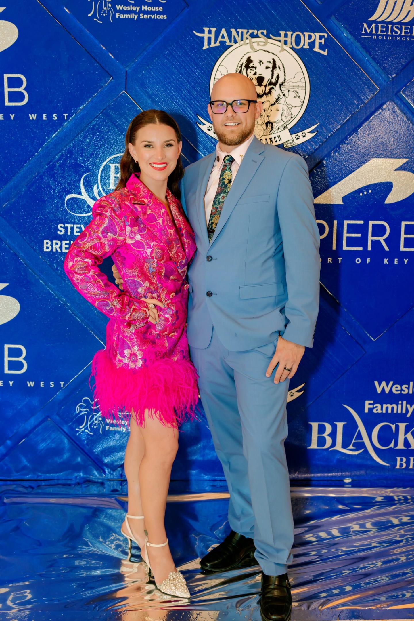 A man in a blue suit and a woman in a bright pink dress, smiling at an event.