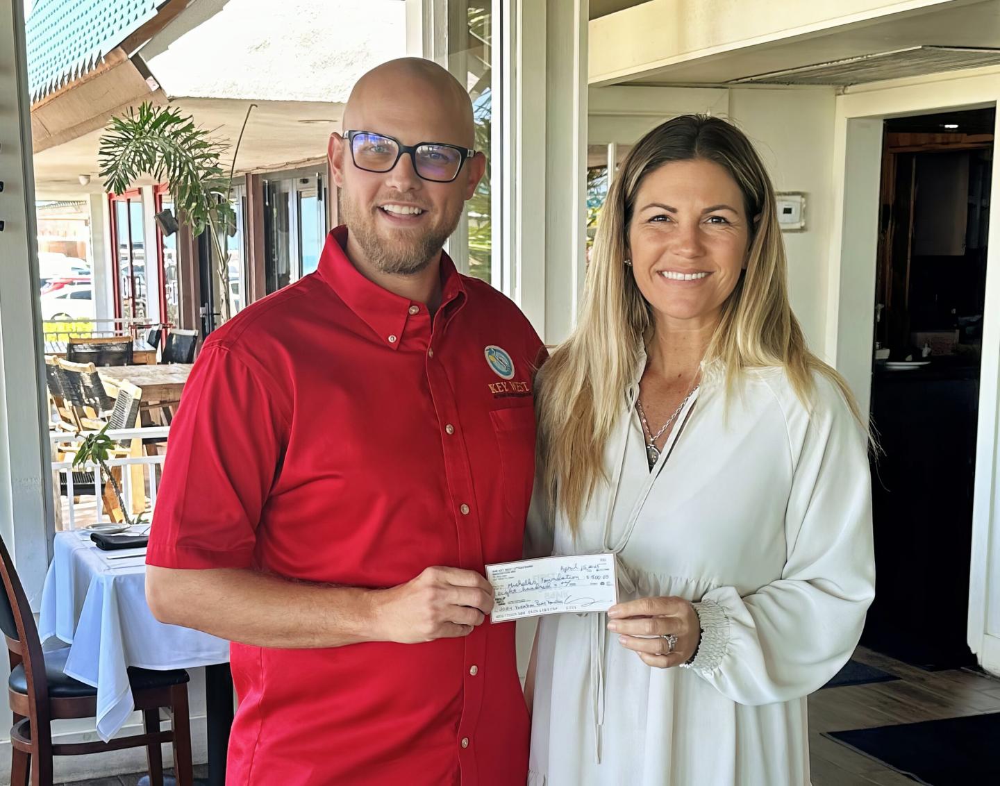 Two people smiling, holding a check in a bright room.