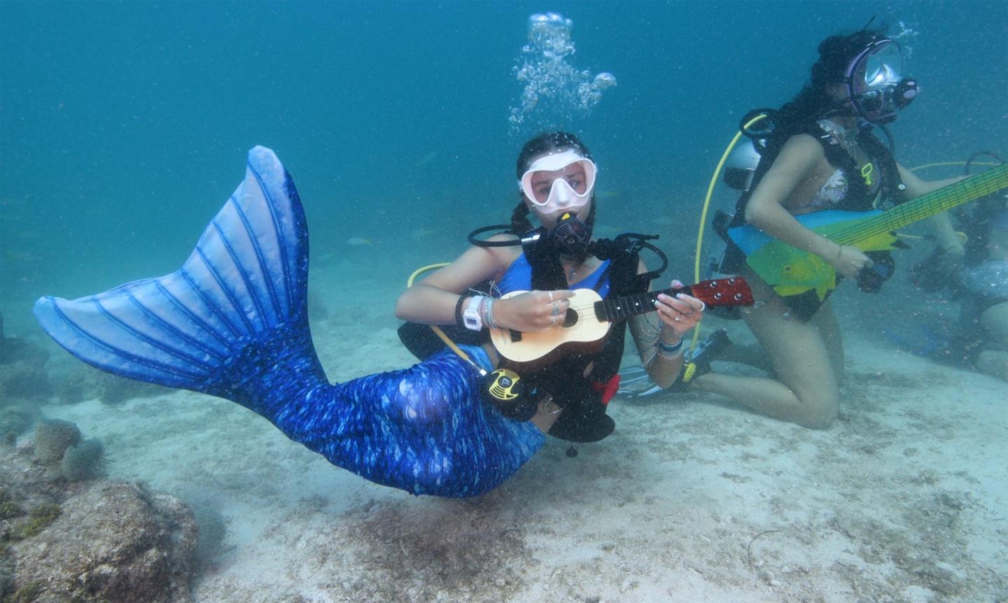 Mermaid and diver playing ukuleles underwater.
