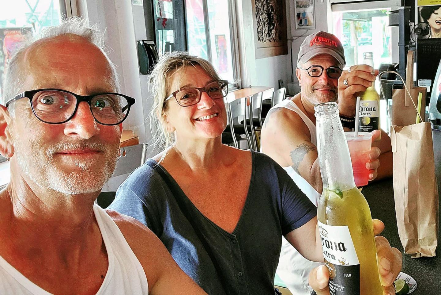 Three people smiling at a bar, each holding a drink.