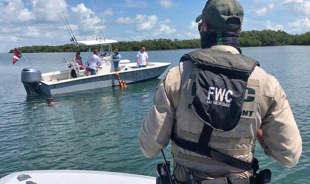 Officer in uniform observes people on a boat in a sunny lake setting.