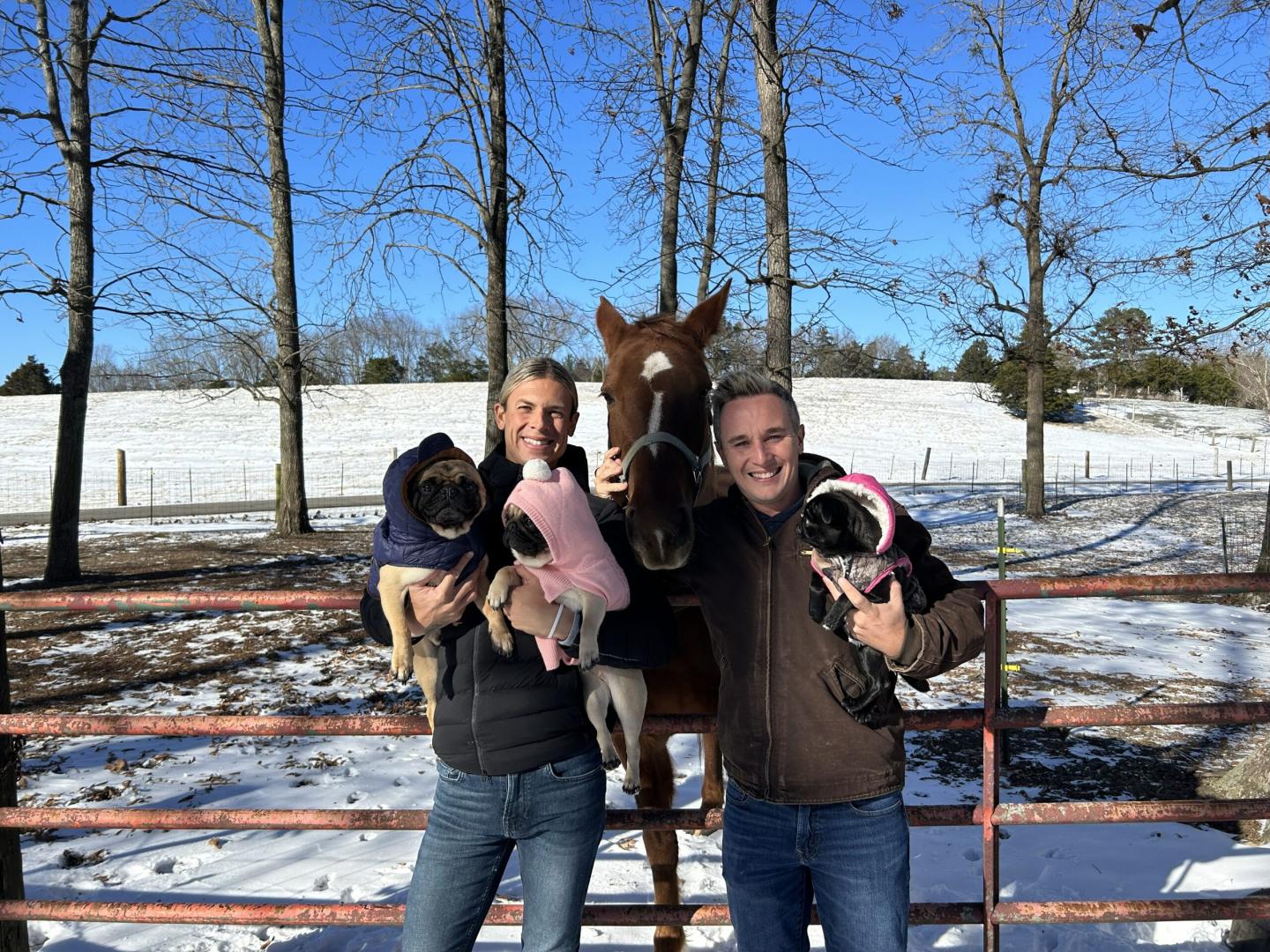Couple with three pugs and a horse in a snowy field.