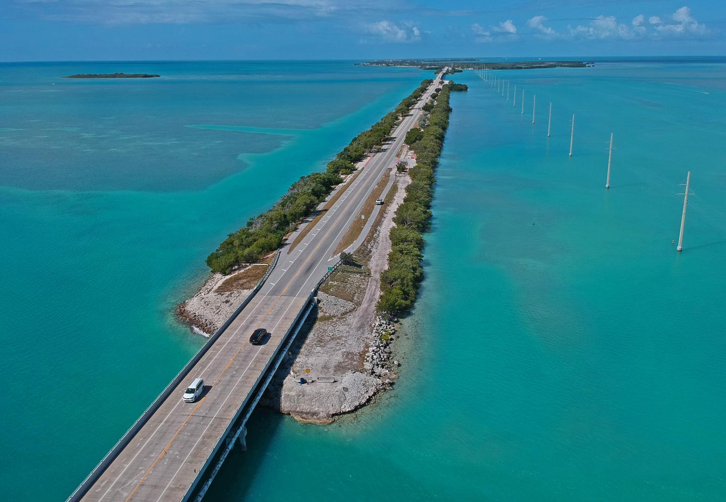 Aerial view of a long highway over turquoise waters with sparse greenery.