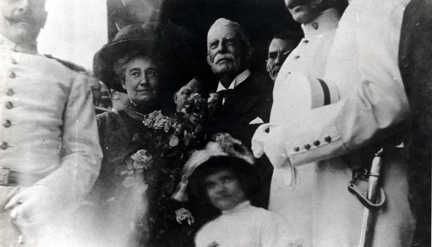Group of people in formal attire, some holding hats and flowers, in a vintage photograph. Henry Flagler and his wife.