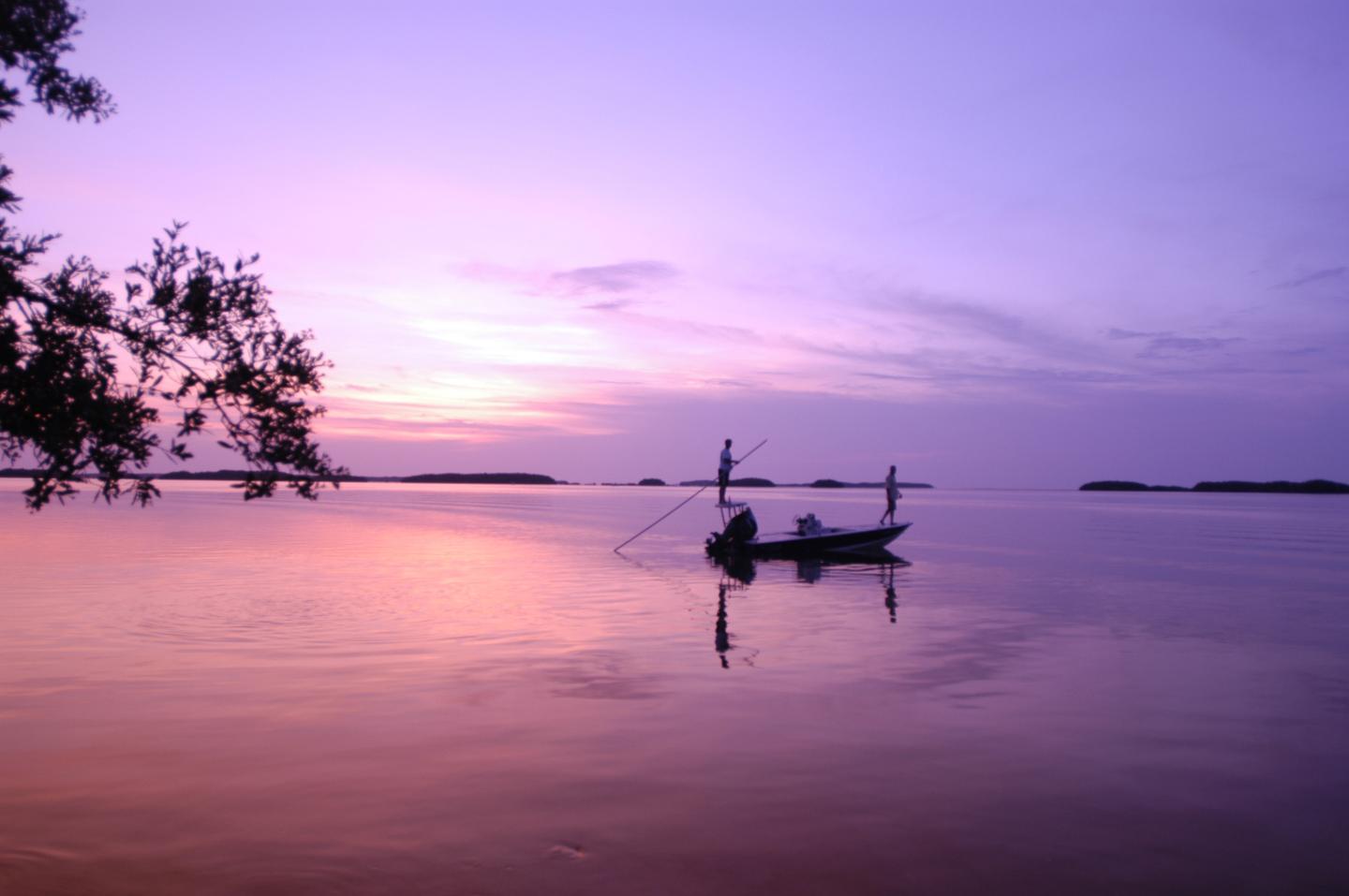 Peaceful sunset over a calm lake with silhouetted boat and trees.