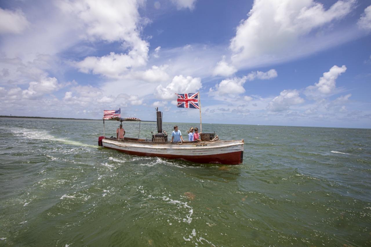 Vintage boat on open water under a cloudy sky with British flags.