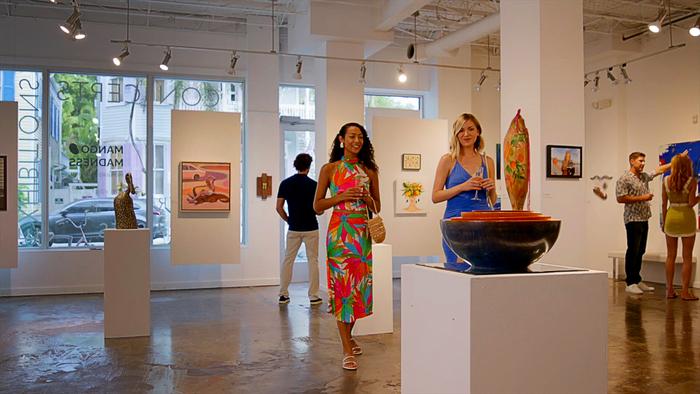 Art gallery with people viewing paintings and sculptures.