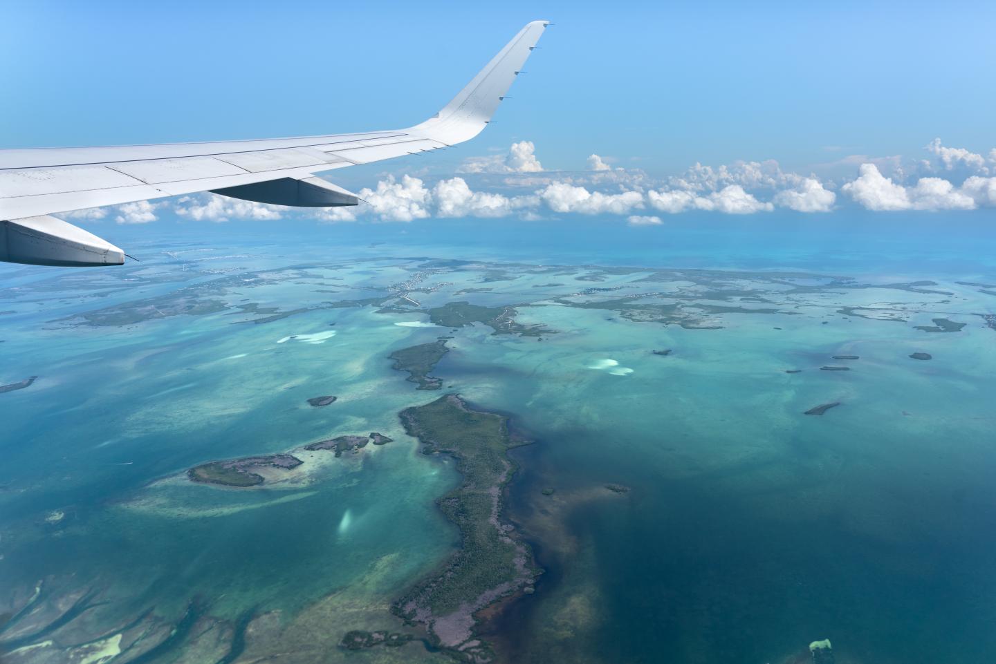Aerial view of islands and turquoise sea, airplane wing visible.