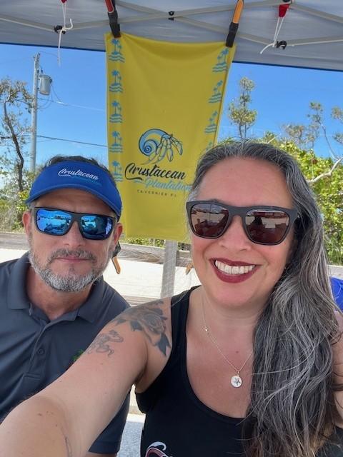 Angela Sayre and husband in sunglasses smiling under a canopy.