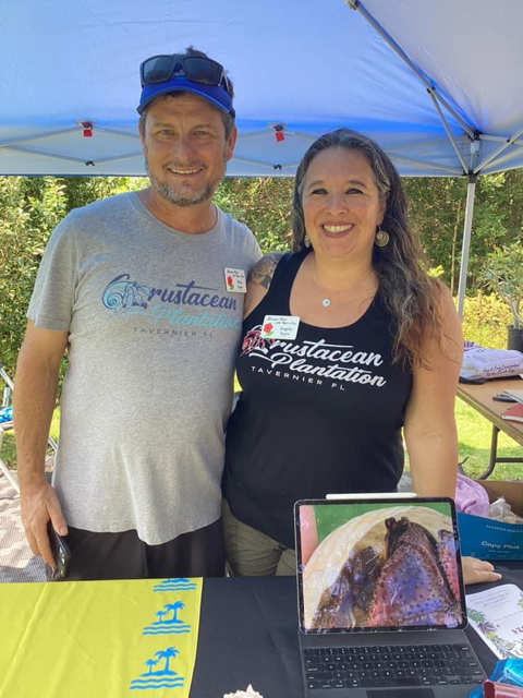 Man and woman smiling under a blue canopy with a laptop displaying food.