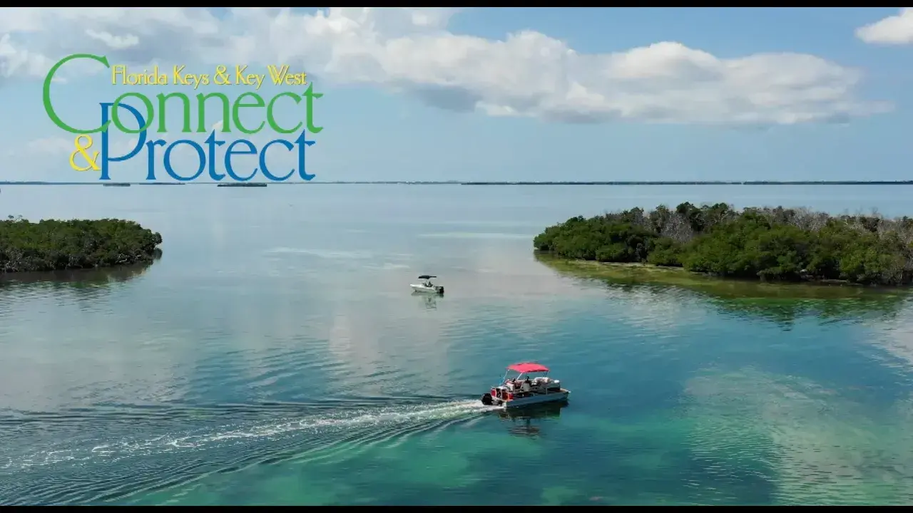 Boats on clear blue water surrounded by lush greenery under a partly cloudy sky.