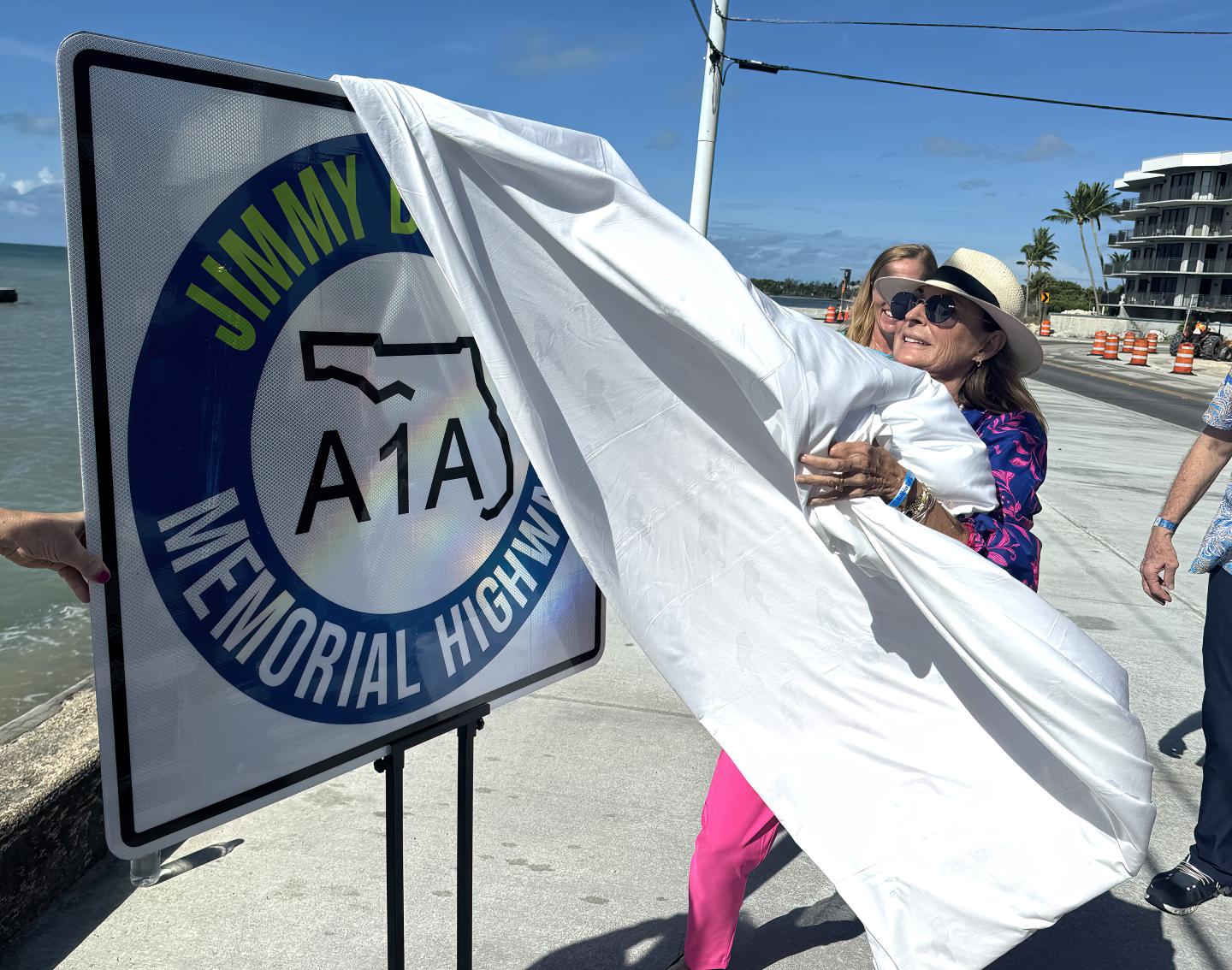 A woman unveils a Jimmy Buffett Memorial Highway sign by the sea.