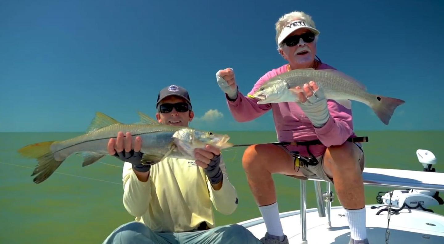 Two people on a boat hold fish under a clear blue sky.