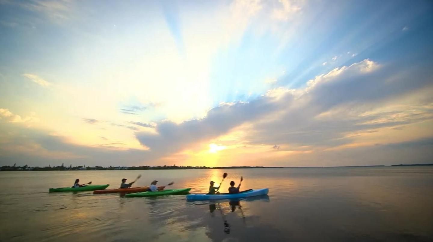 Kayakers paddling on a Florida Keys waters at sunset under a sky with radiant clouds.