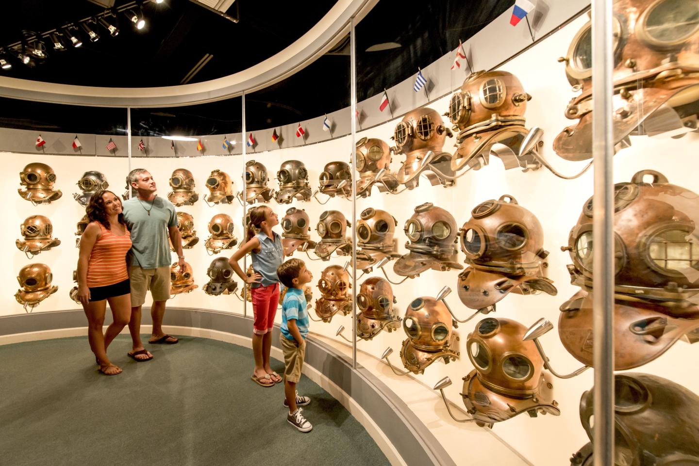 Family admires vintage diving helmets in a well-lit museum exhibit.