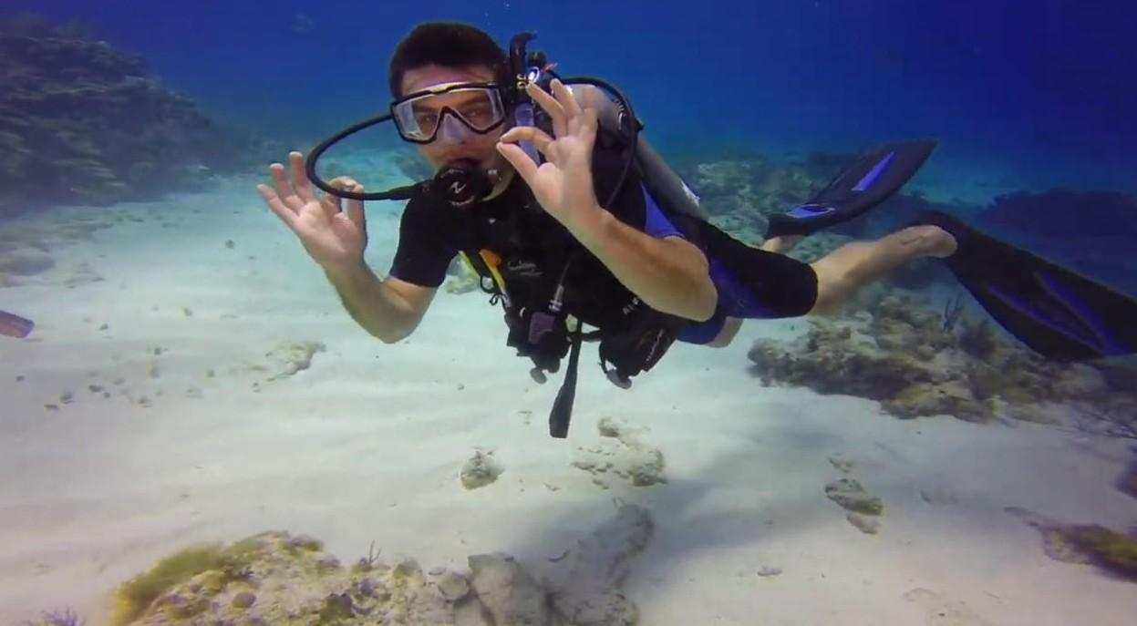 Scuba diver underwater giving an OK sign near sandy ocean floor.