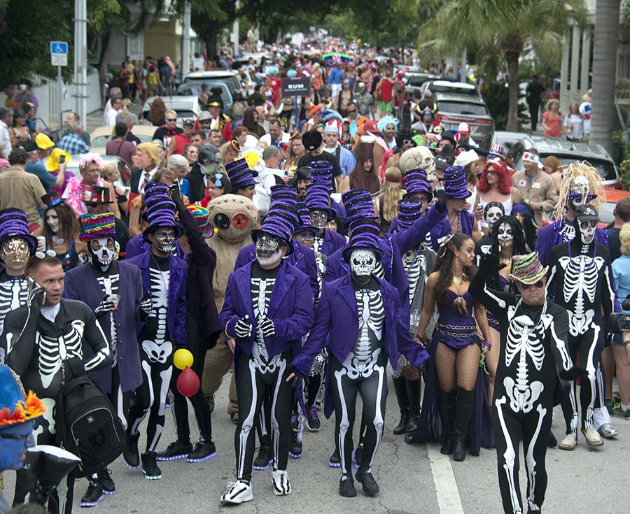 Parade with people in skeleton costumes and vibrant purple attire on a crowded street.