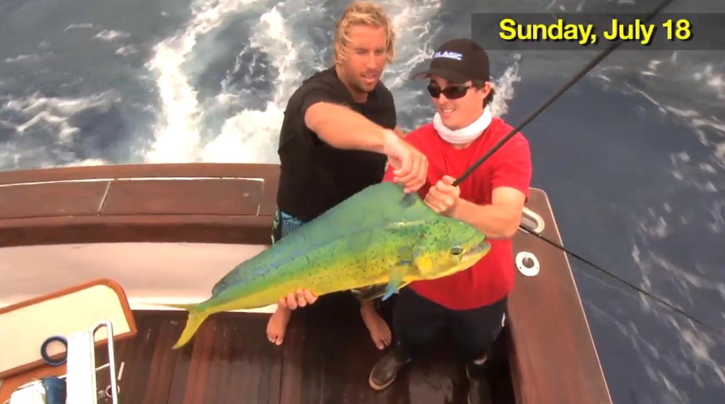 Two men holding a large mahi mahi fish on a boat.