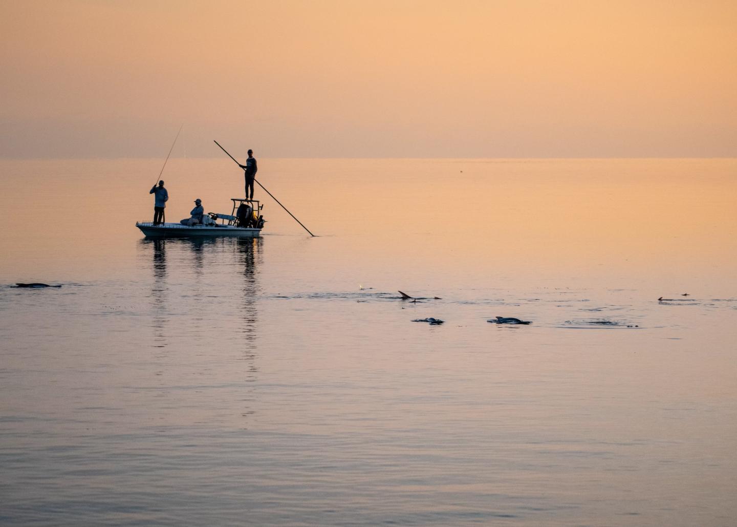 Boat on calm water at sunset, people fishing, and gentle ripples.
