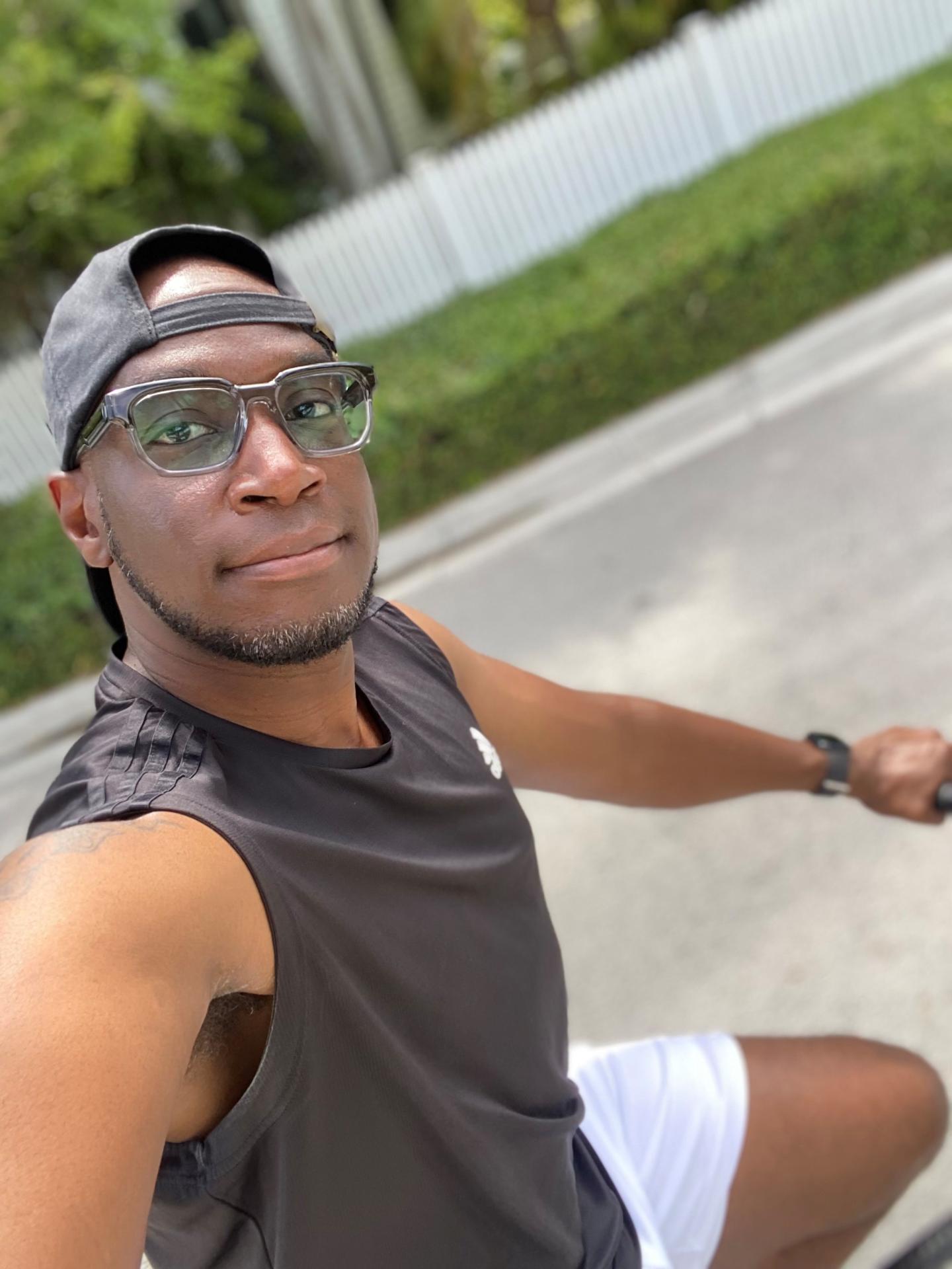 Floyd "Pepa" Jenkins riding a bike, wearing a cap and glasses, on a sunny day.