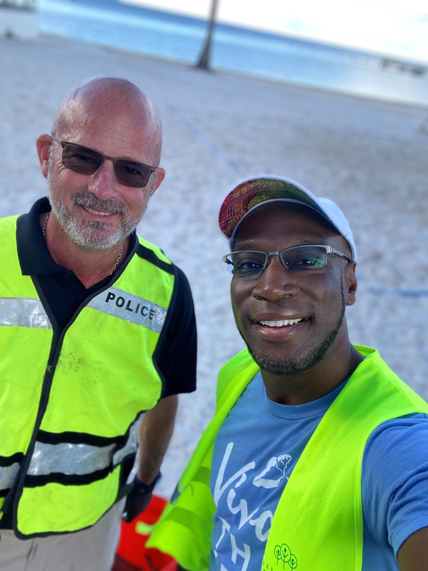 Two men in yellow vests smiling on a beach.