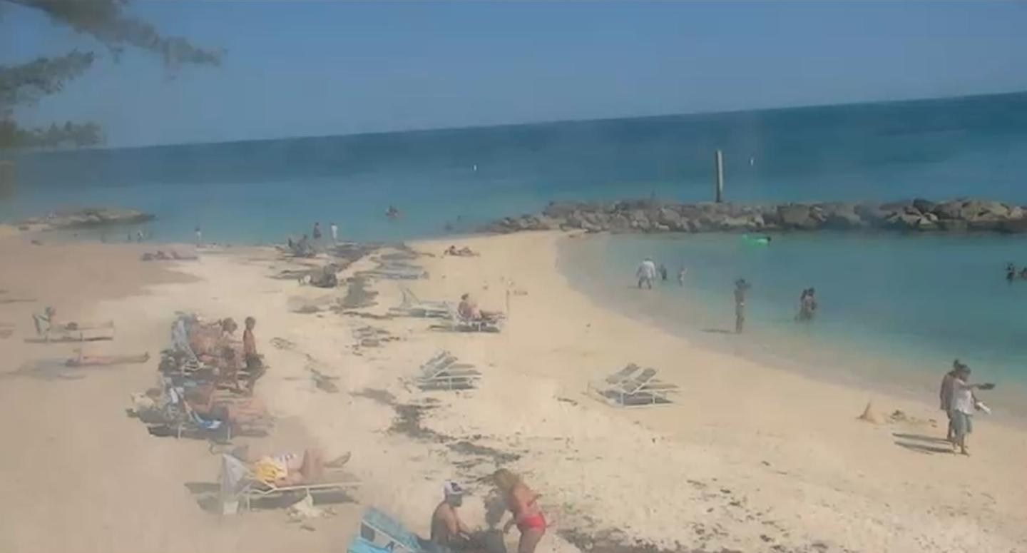 Beach scene with people relaxing and swimming in the blue ocean.