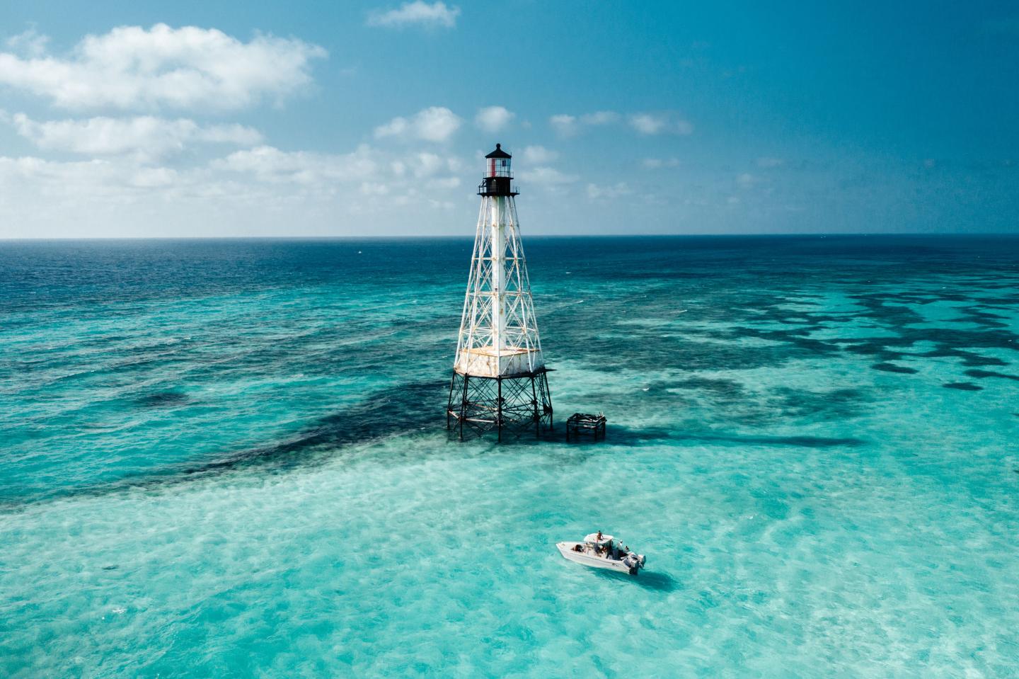 Towering lighthouse over clear turquoise sea, with a small boat nearby.