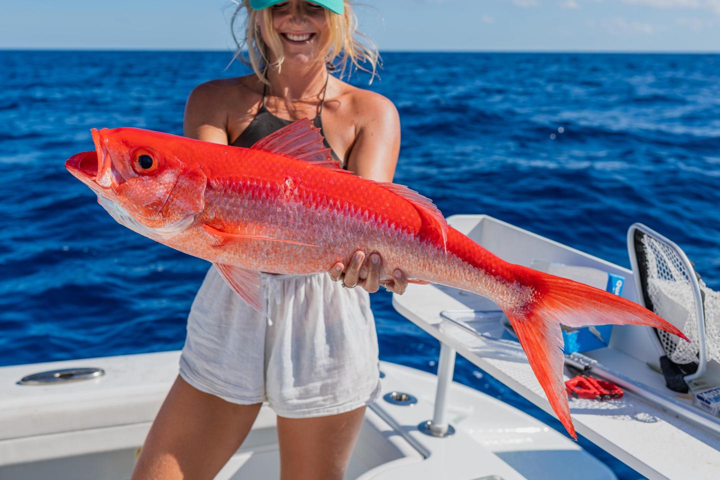 Smiling person holds a large red fish on a boat against the ocean backdrop.